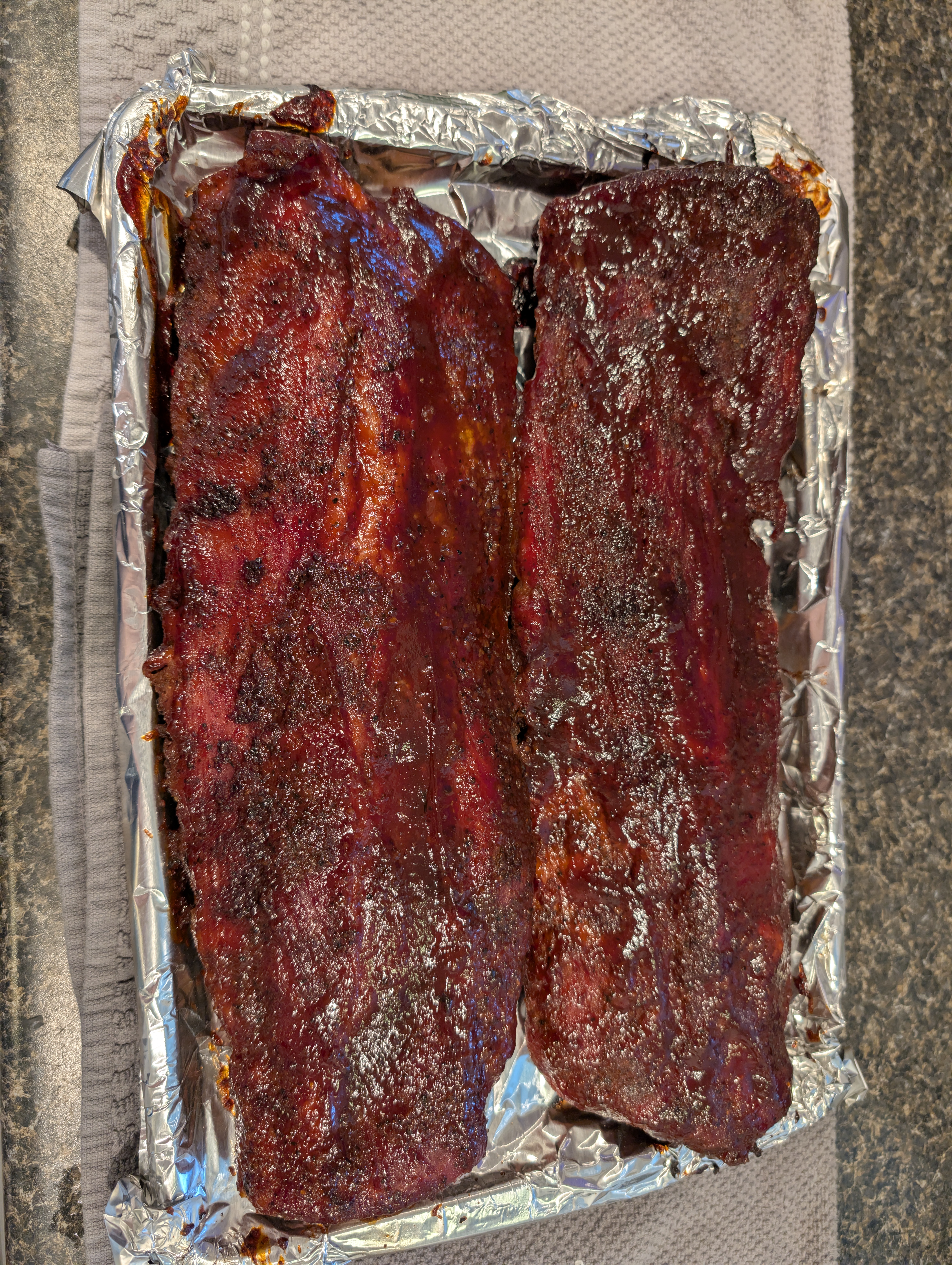 Wrapped and glazed ribs resting in a foil pan