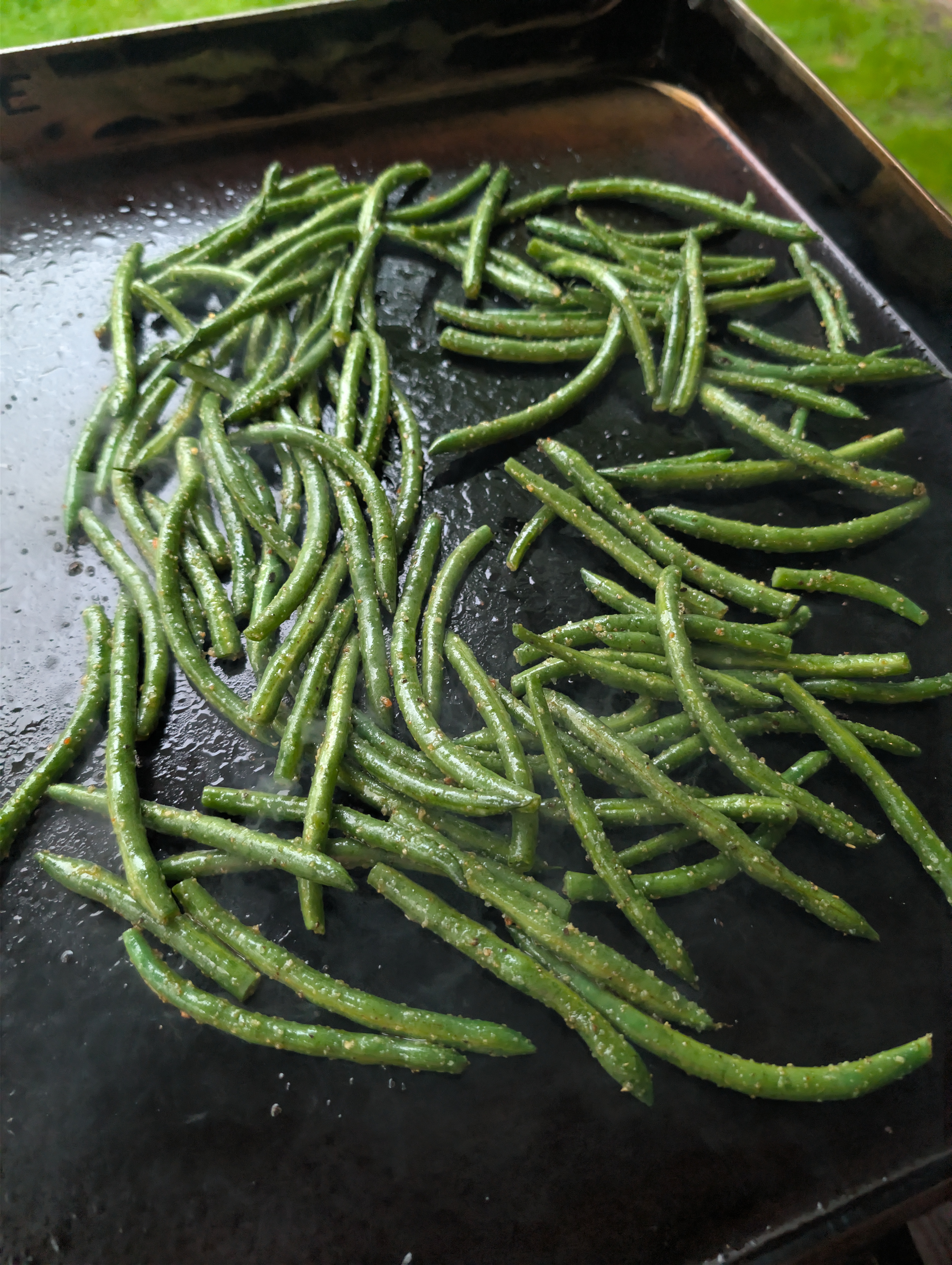 Seasoned green beans spread on a flat top griddle before cooking