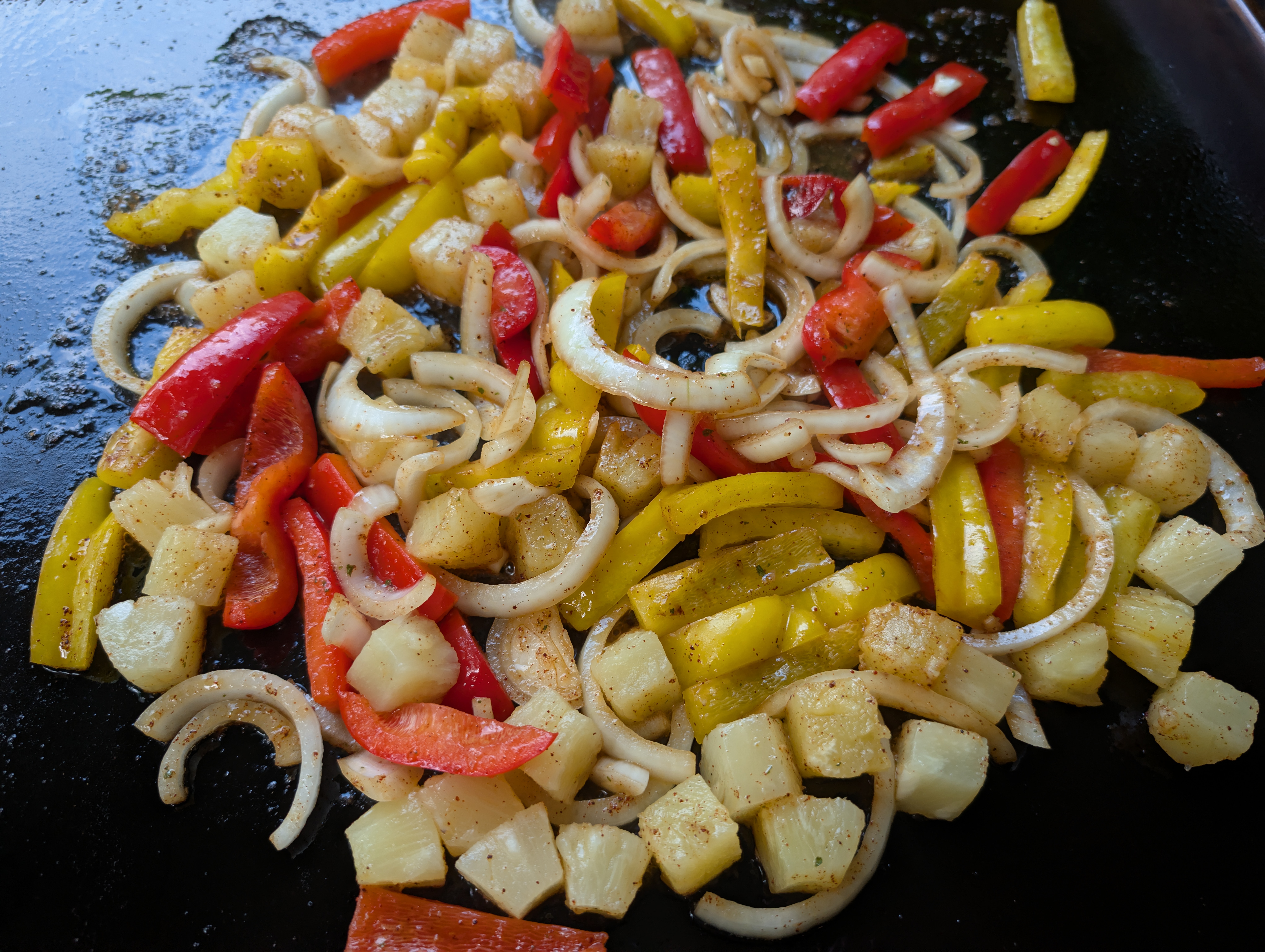 Onions, colored peppers, and pineapple chunks cooking on the Blackstone griddle